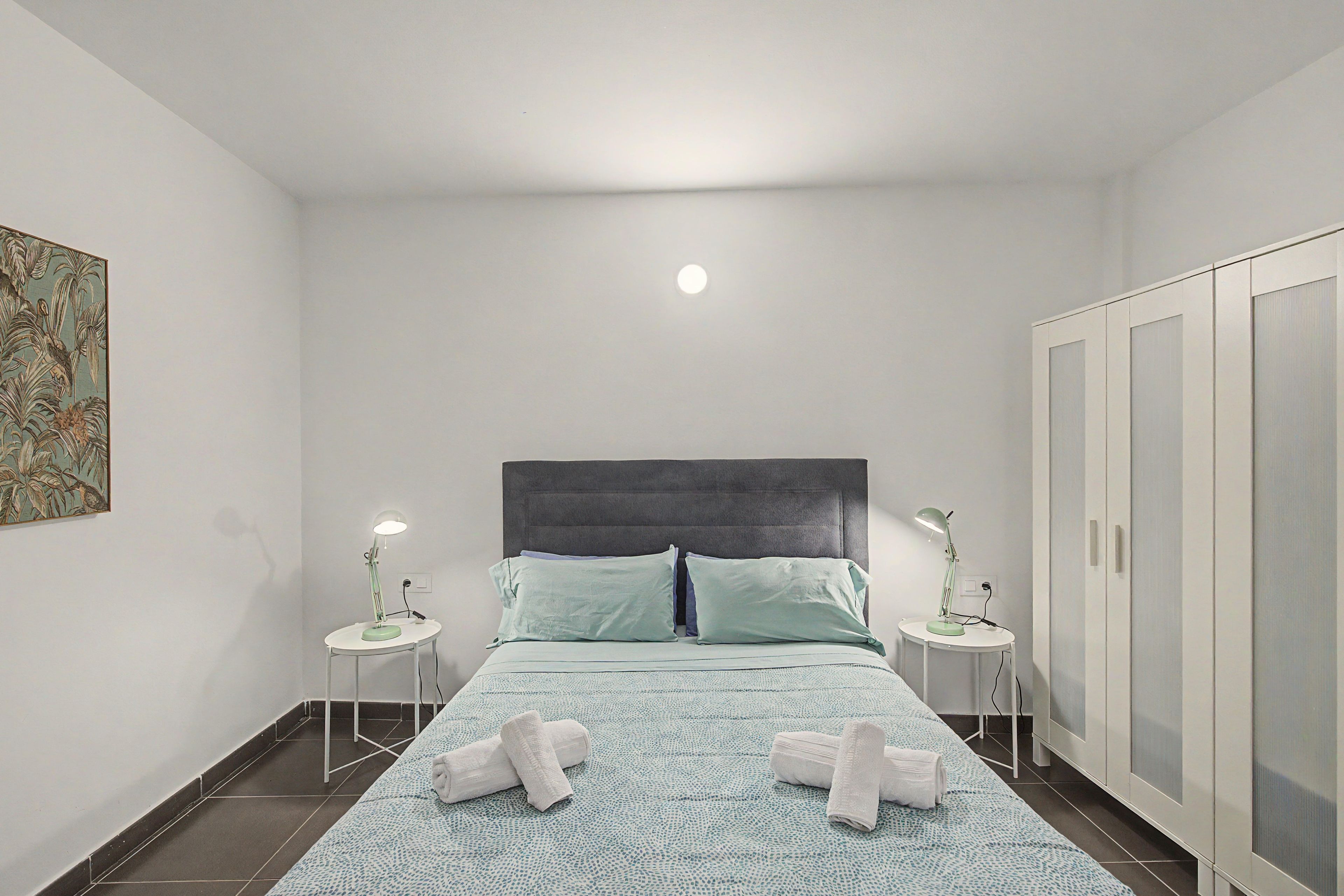 Ein Schlafzimmer mit einem Bett, zwei Nachttischen, einem Kleiderschrank und einem Bild an der Wand.