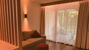 Ein modernes Wohnzimmer mit einer Couch, einem roten Hocker und einem großen Fenster mit leichtem Vorhang.