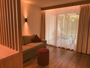 A modern living room with a sofa, a red ottoman, and a large window with sheer curtains. - Apartment at Hotel and Residences Theresia with Mountain View and Private Terrace (St. Leonhard in Passeier)