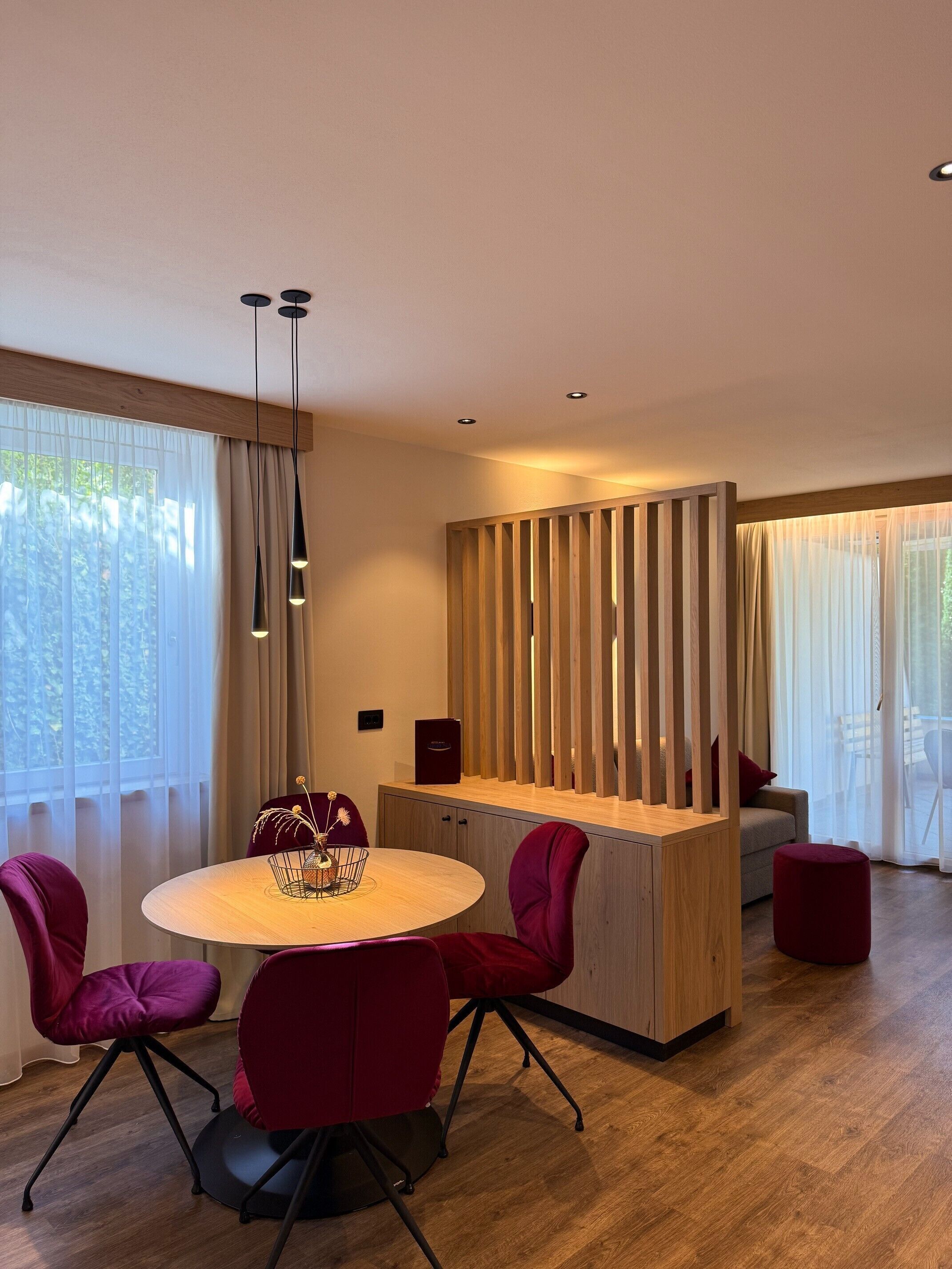 A modern dining area with a round table, red chairs, a wooden cabinet, and a kitchen area with a wooden partition.