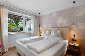 A hotel room with a large bed, a window with curtains, a wall with a floral pattern, and a bedside table with a lamp. - Apartment at Hotel and Residences Theresia with Mountain View and Private Terrace (St. Leonhard in Passeier)