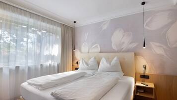 Ein Hotelzimmer mit einem großen Bett, zwei Nachttischen, einer Wandlampe und durchscheinenden Vorhängen.