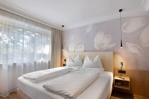 Ein Hotelzimmer mit einem großen Bett, zwei Nachttischen, einer Wandlampe und durchscheinenden Vorhängen.