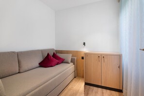 Un canapé de couleur neutre, agrémenté d’un coussin, et un meuble en bois doté de deux portes.