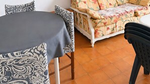 Une pièce comprenant une table à manger, un canapé recouvert d’un tissu à motifs floraux, un miroir à cadre en bois et un téléviseur posé sur un meuble en bois.