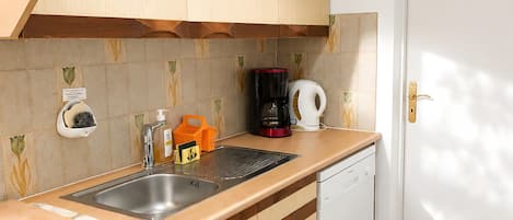 Uma cozinha com armários de madeira, uma pia de aço inoxidável, uma cafeteira e uma máquina de lavar louça.
