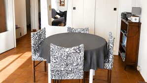 Un coin repas avec une table ronde, des chaises à motifs, un meuble contenant des livres et une porte donnant sur une autre pièce.