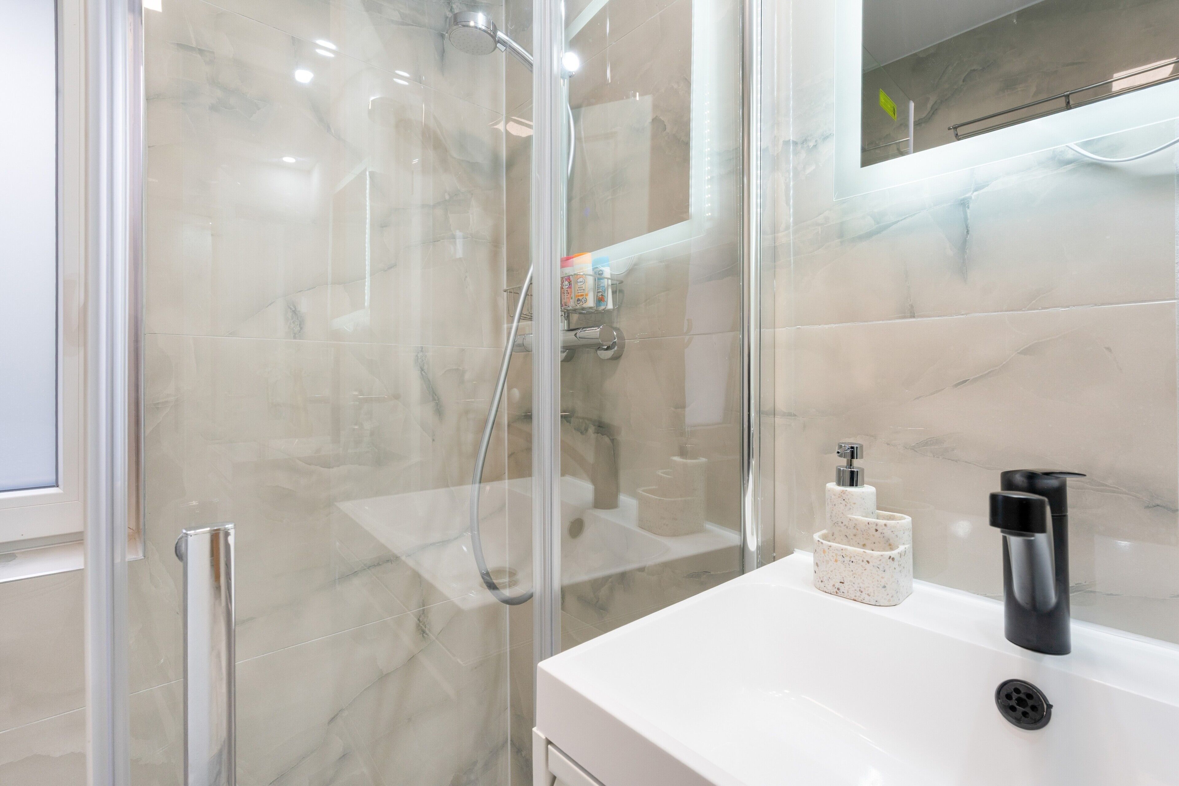 A modern bathroom with a glass shower enclosure, a white sink, and a mirror.