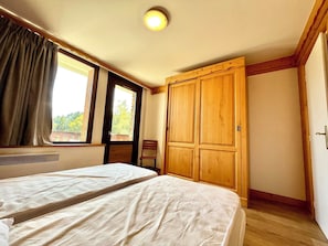A bedroom with two beds, a wooden wardrobe, a window with curtains, and a radiator. - Reflection of Mont Blanc (Combloux)