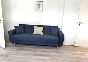 Un canapé bleu foncé avec un coussin de couleur claire, dans une pièce dotée d’un parquet en bois clair et de murs blancs.