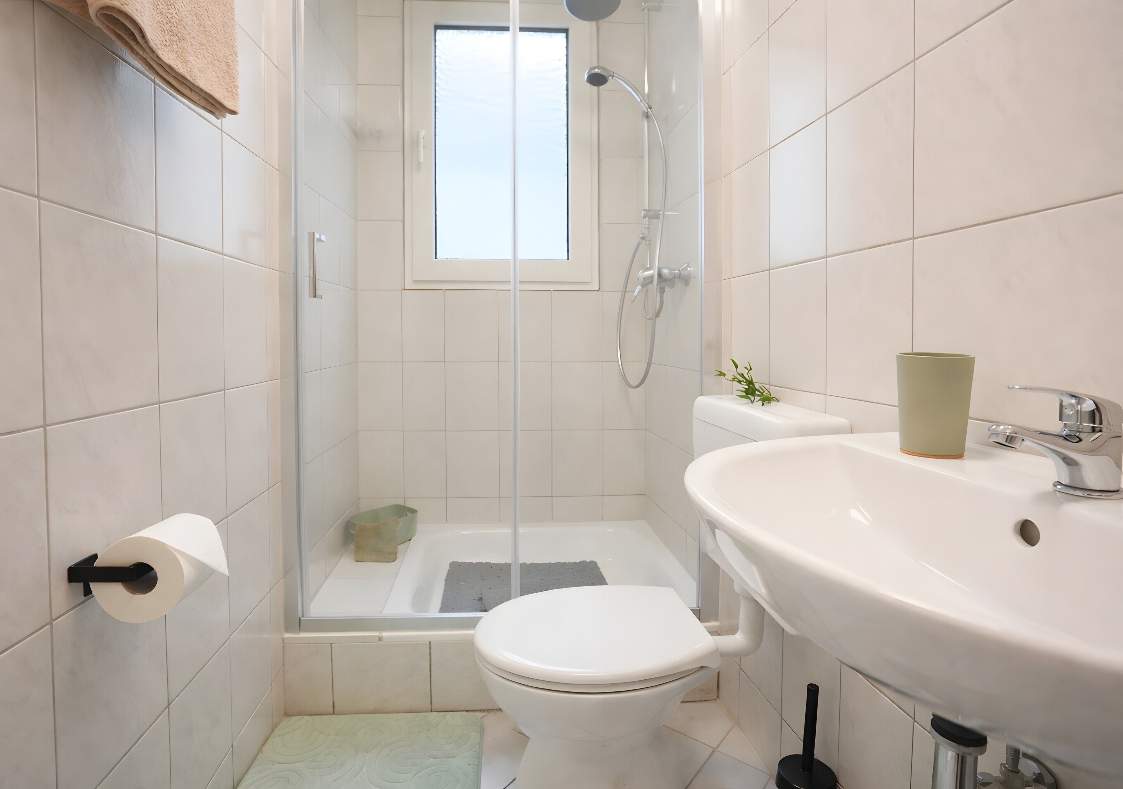 A bathroom with a toilet, sink, shower, and a window.