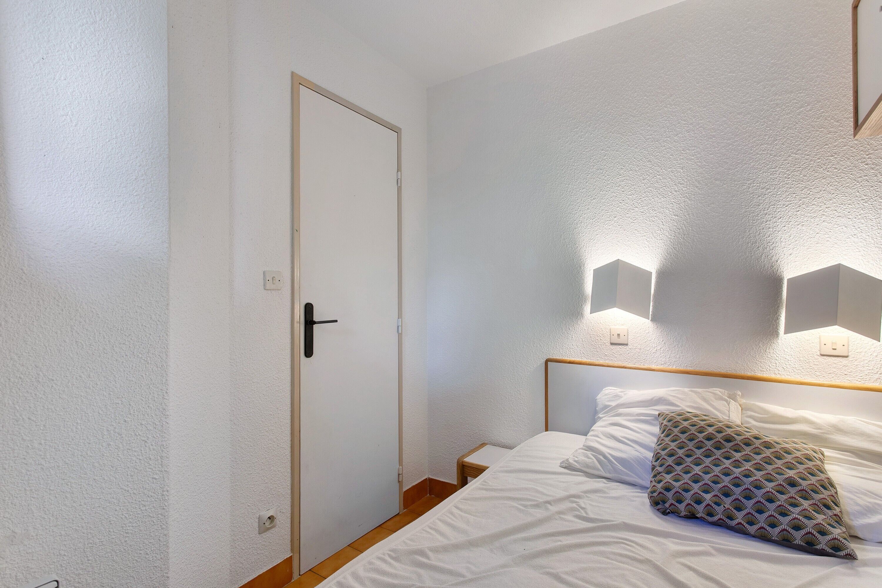 A bedroom with a single bed, a door, and wall-mounted lights.