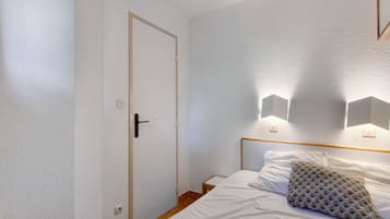 A bedroom with a single bed, a door, and wall-mounted lights.
