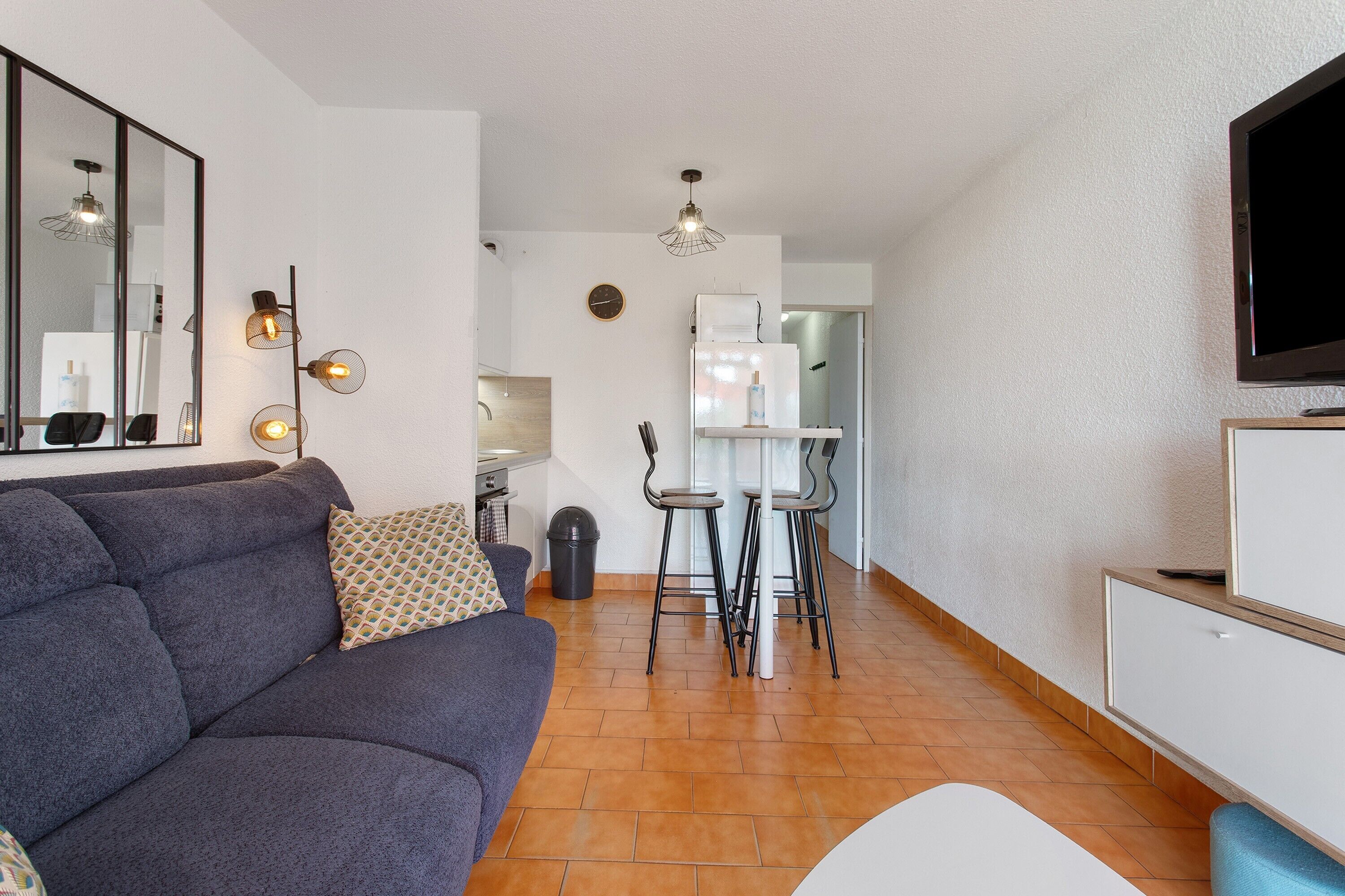 A modern living room with a sofa, a TV, and a dining area with chairs and a table.