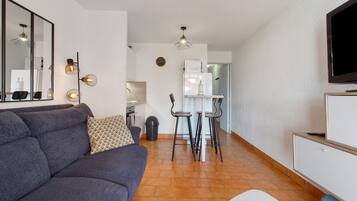 A modern living room with a sofa, a TV, and a dining area with chairs and a table.