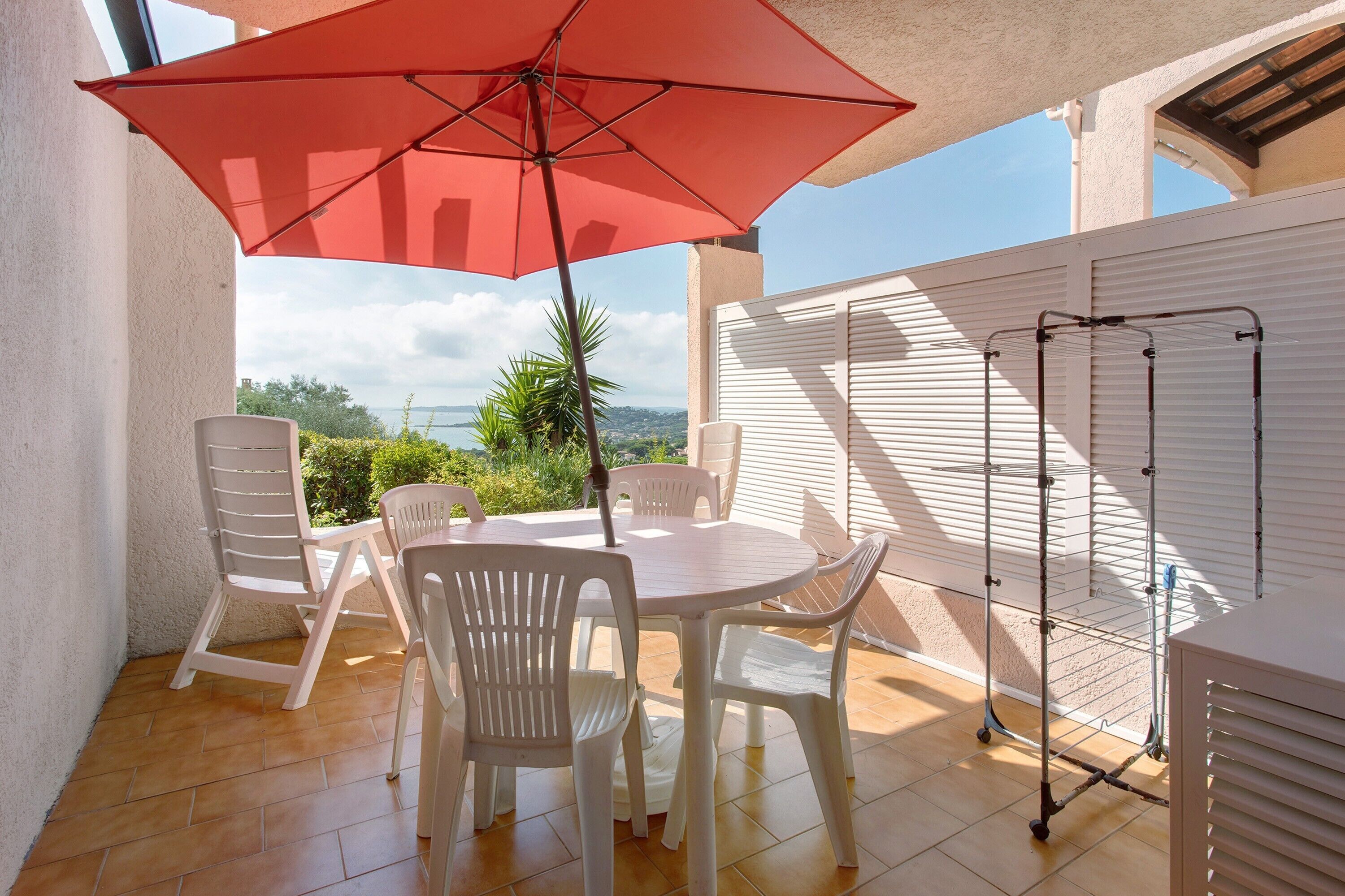 Une terrasse avec une table et des chaises, un parasol rouge et un étendoir à linge.
