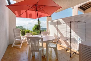 A patio with a table and chairs, a red umbrella, and a clothes drying rack. - Apartment '2 Pièces Sainte Maxime' with Sea View, Shared Pool and Wi-Fi (Sainte-Maxime)