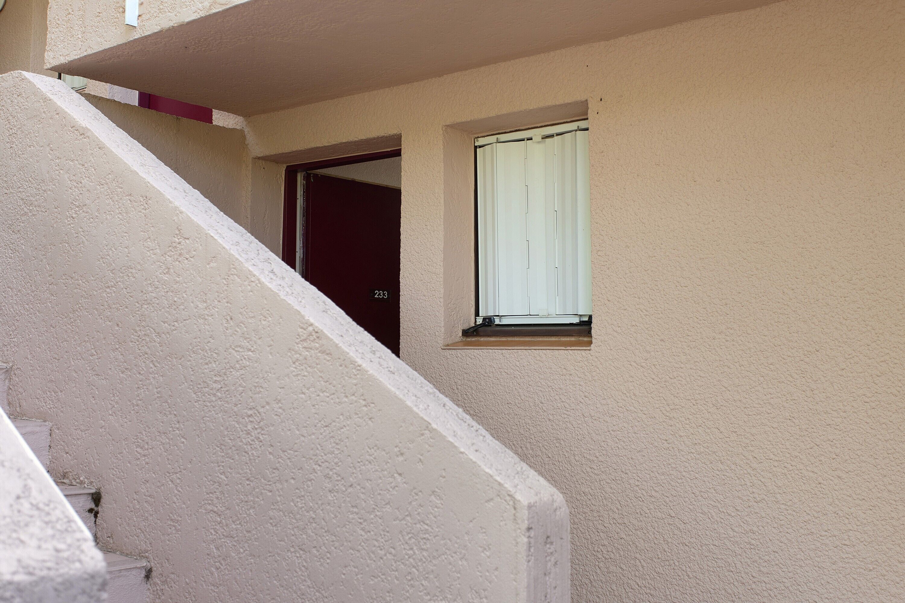 A residential building with a beige exterior, a visible door, and a window with a white blind.