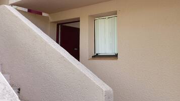 A residential building with a beige exterior, a visible door, and a window with a white blind.