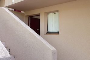 Un immeuble résidentiel à la façade beige, avec une porte bien visible et une fenêtre dotée d’un store blanc.
