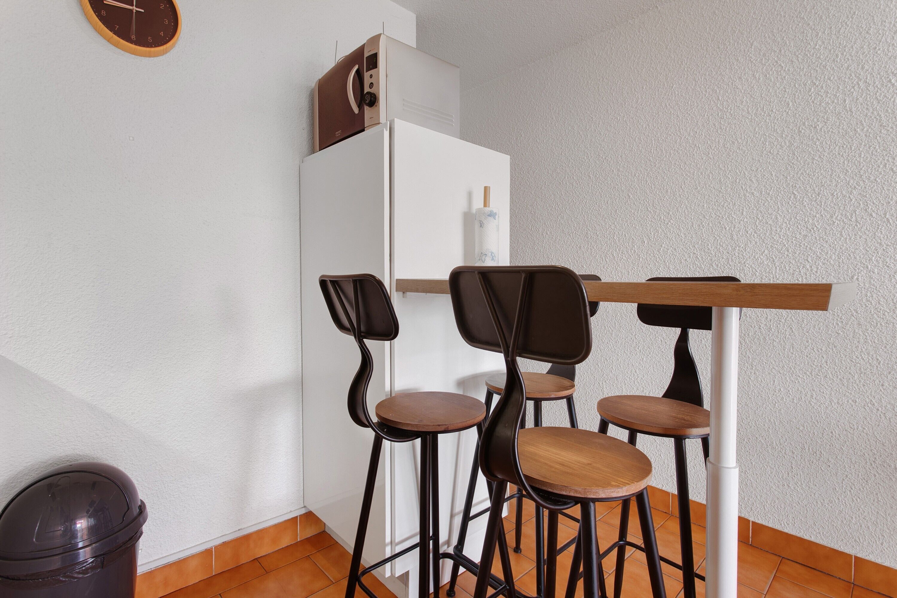 Una kitchenette equipada con microondas, refrigerador y una mesa de madera con cuatro sillas.