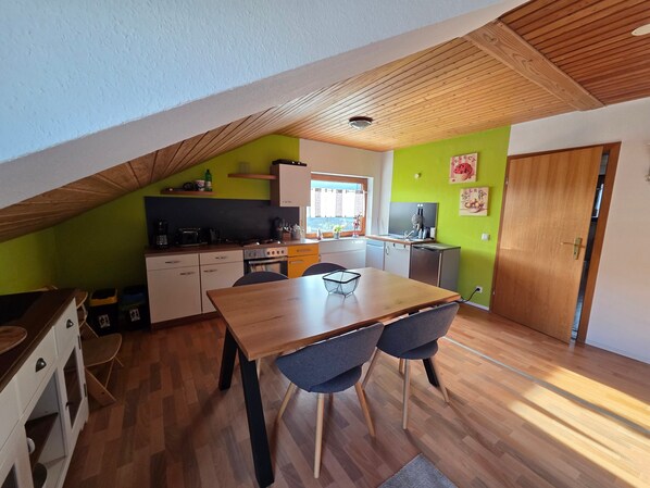 A compact kitchen with a dining area, wooden ceiling, and green walls.