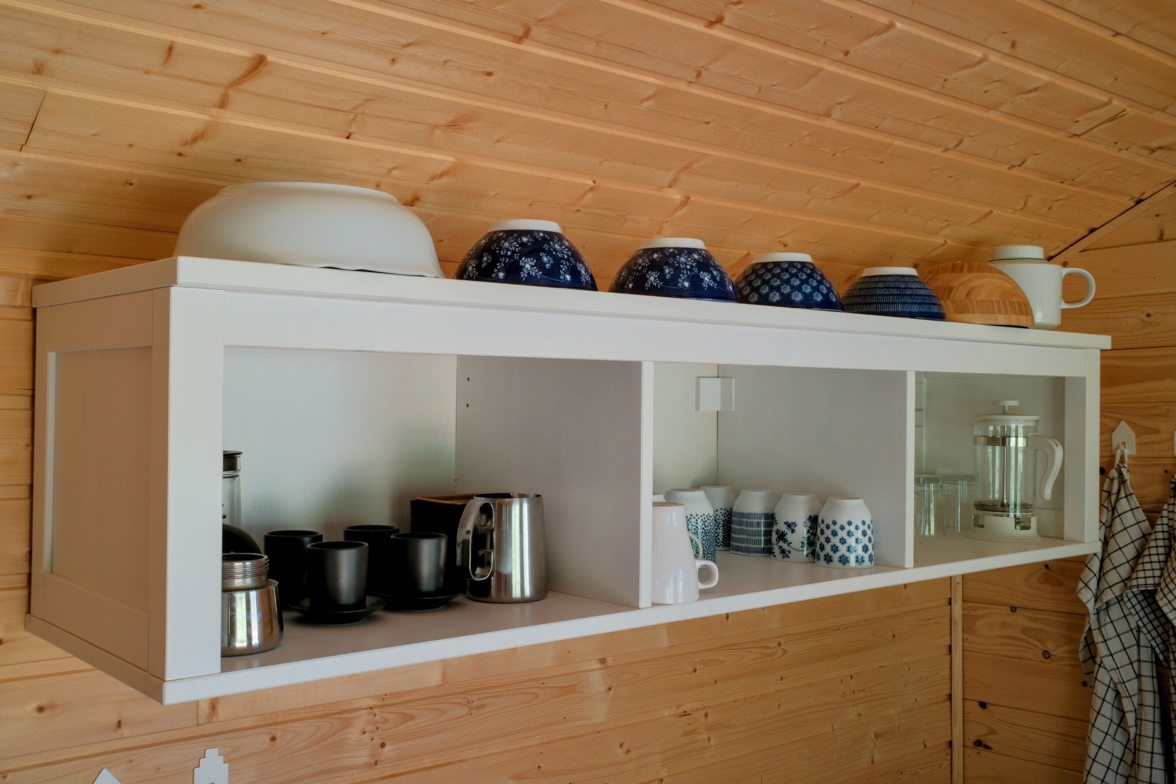 A white shelf with various kitchenware including mugs, a coffee pot, and a teapot.