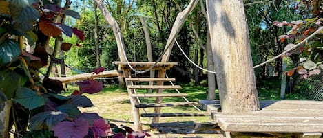 A wooden climbing structure in a natural setting with ropes and platforms.