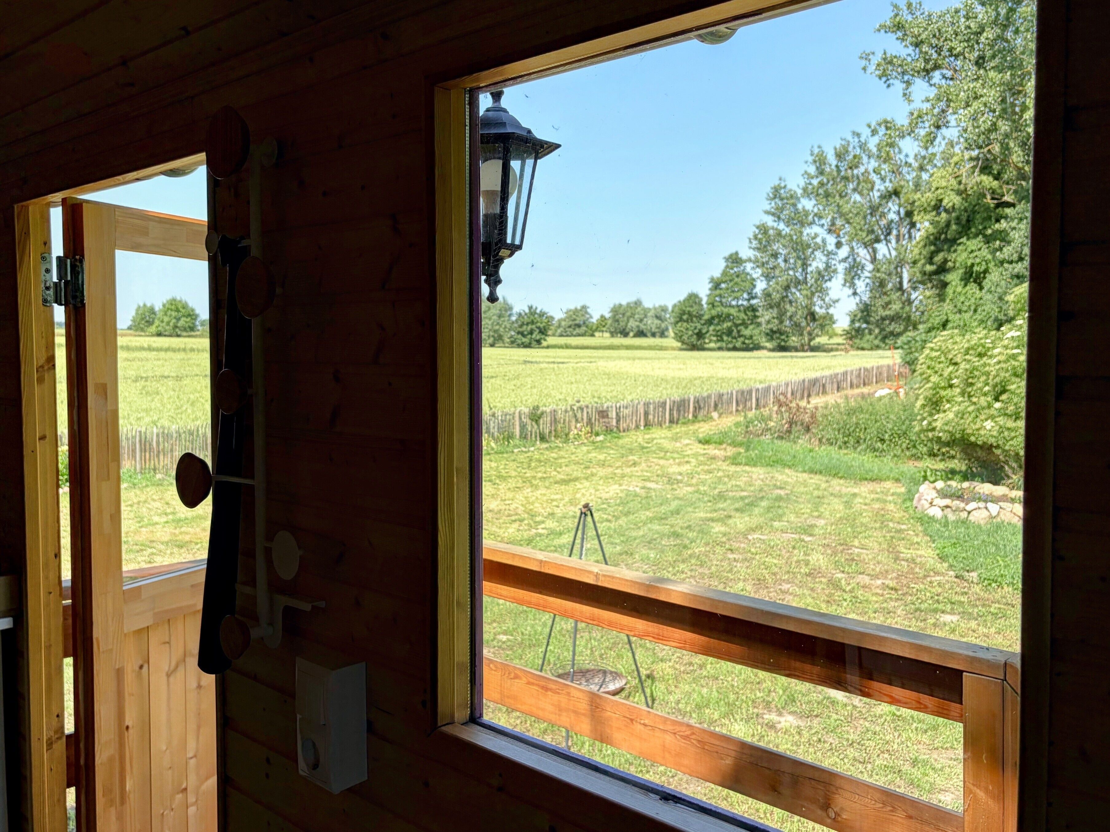 Une cabane en bois dotée d’une grande fenêtre donnant sur un champ verdoyant et des arbres.