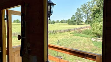 Une cabane en bois dotée d’une grande fenêtre donnant sur un champ verdoyant et des arbres.