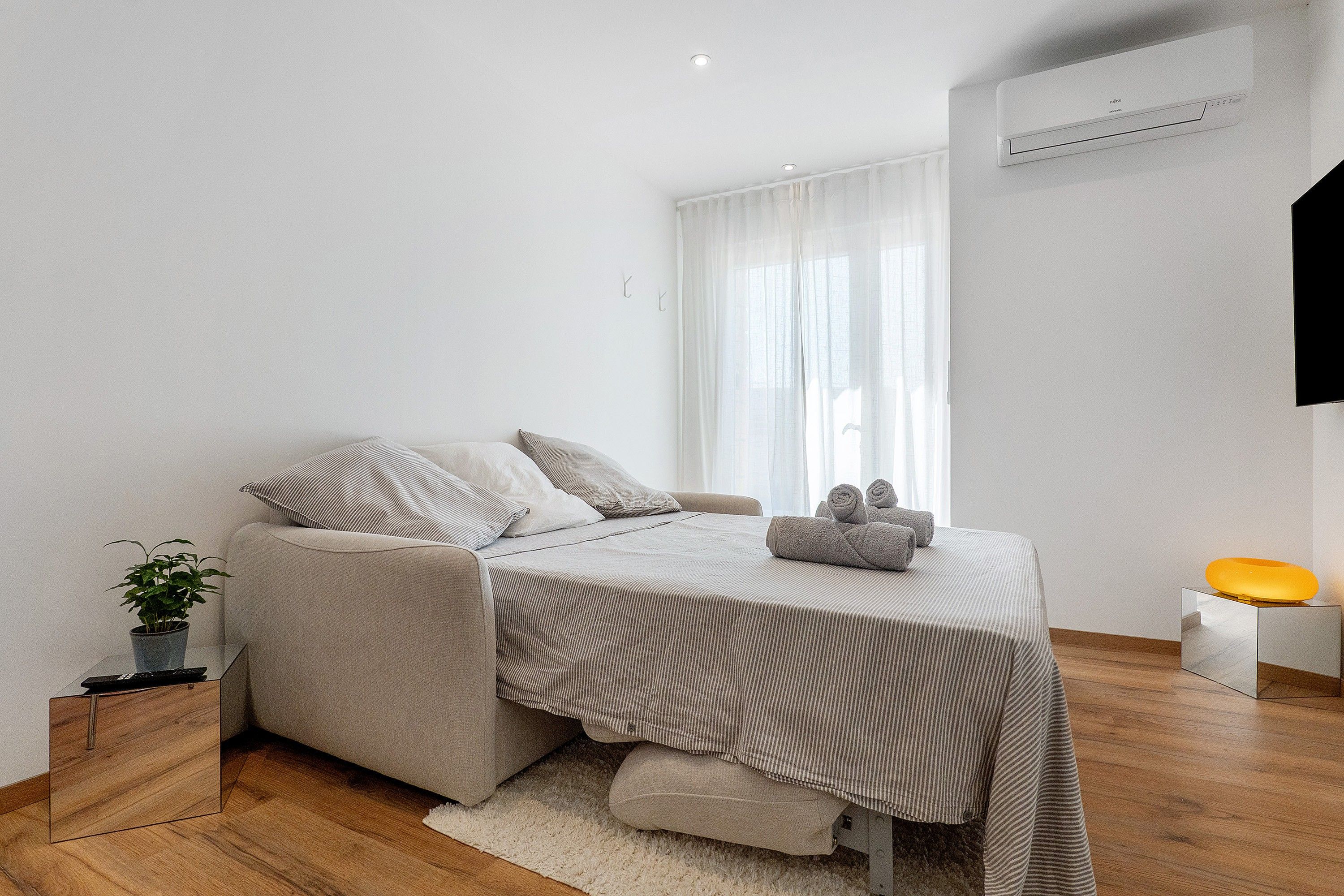 Een moderne slaapkamer met een bed, nachtkastje, een potplant en een airconditioner.