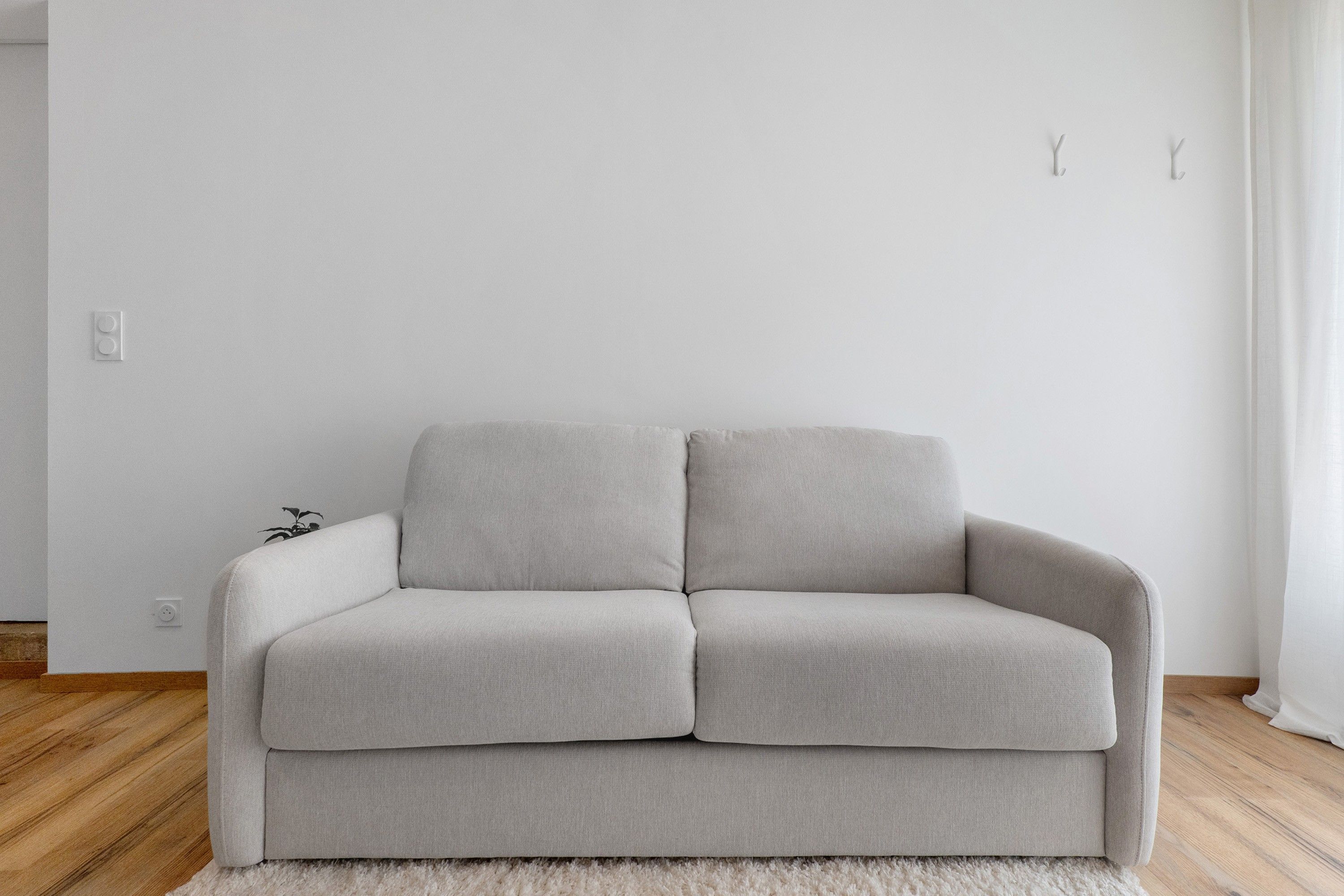 Ein ansprechendes, neutrales Sofa in einem minimalistischen Raum mit Holzboden und weißem Teppich.