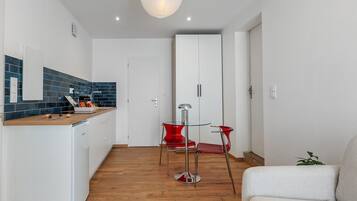 Une cuisine moderne avec un plan de travail en bois, un coin repas avec une table en verre et des chaises rouges, et une armoire blanche en arrière-plan.
