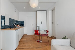 Et moderne køkken med træbordplade, et spiseområde med et glasbord og røde stole, og et hvidt skab i baggrunden.