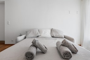 A neatly made bed with rolled towels, a striped bedspread, and two pillows. - Fully Equipped Provence Studio with Mountain View, Wi-Fi, and Air Conditioning (Volonne)