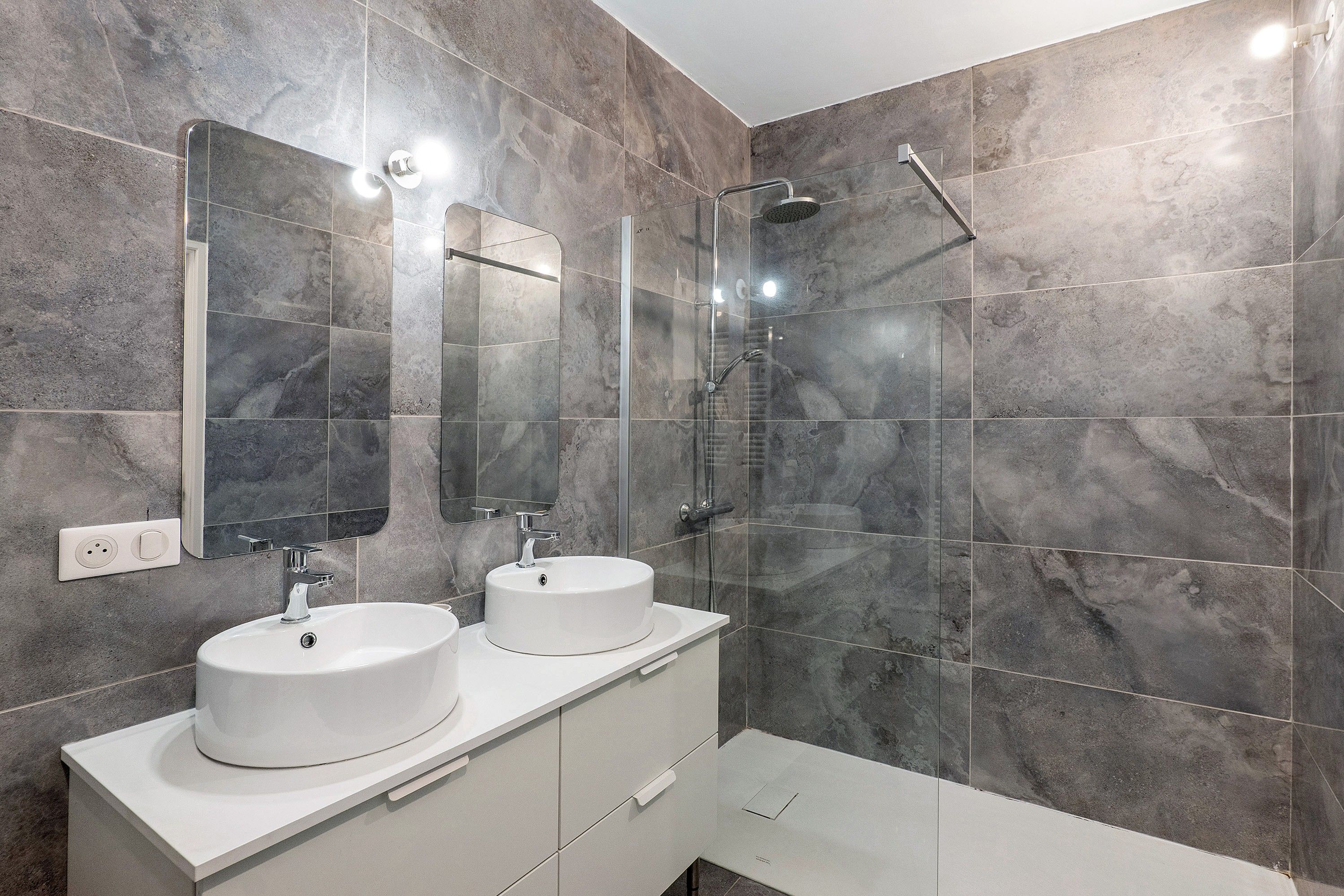 Une salle de bain moderne avec deux lavabos, une douche et un grand miroir.