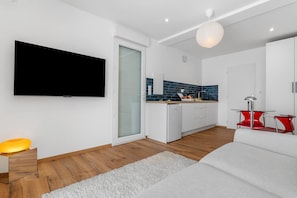 A modern kitchen with a built-in oven, a dining area with a red chair, and a large flat-screen TV mounted on the wall.