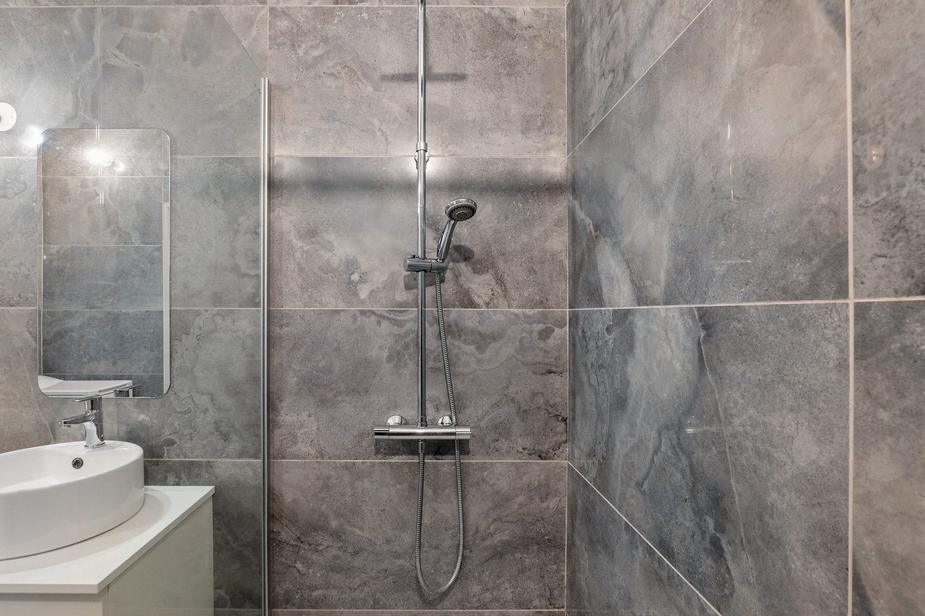 Une salle de bain moderne avec une douche, un lavabo et un miroir.