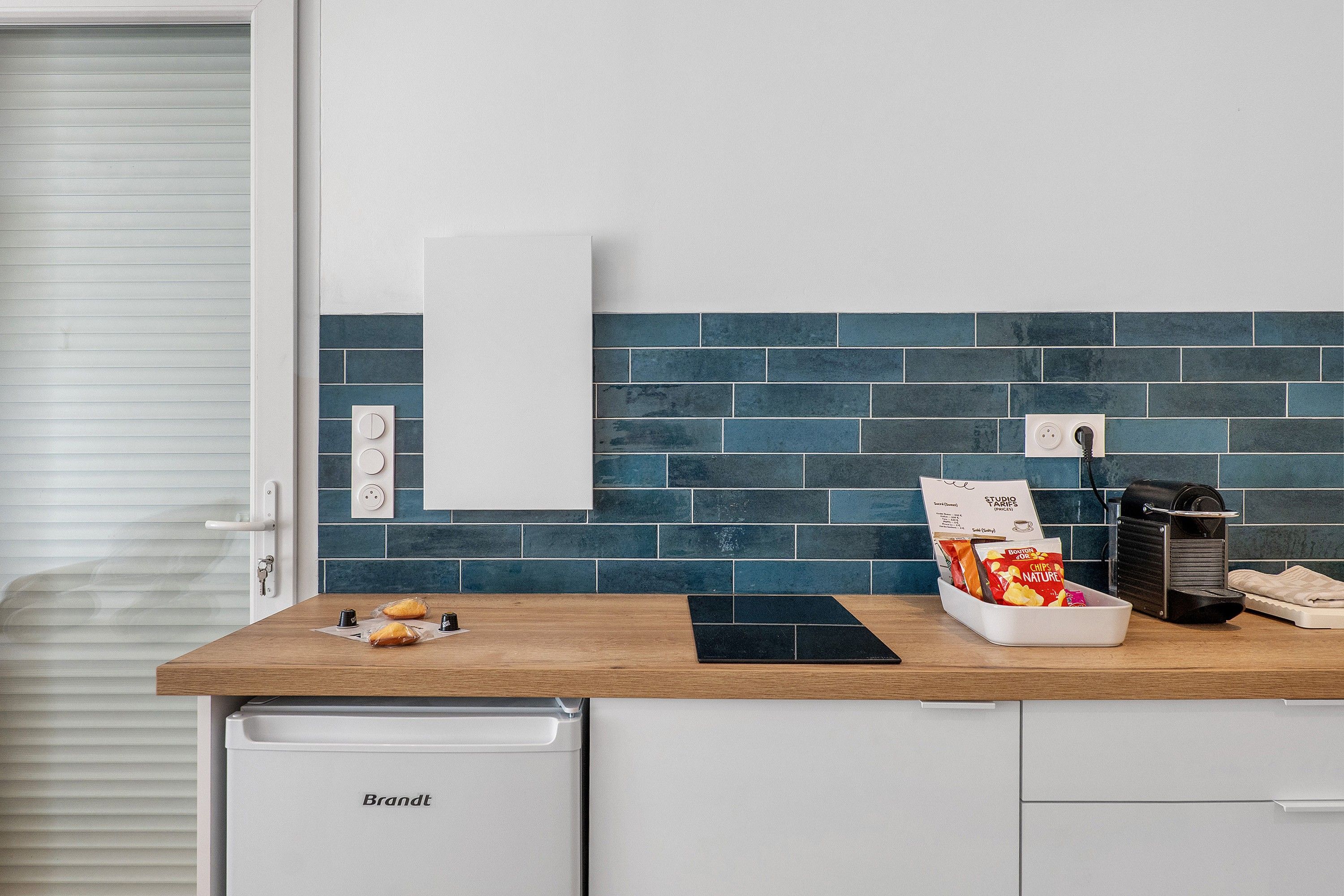 Cozinha com bancada de madeira, armário branco e painel de azulejos azuis, além de uma cafeteira.