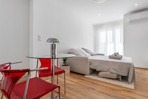 A modern bedroom with a glass table, red chairs, a bed with a striped blanket, and a window with sheer curtains.