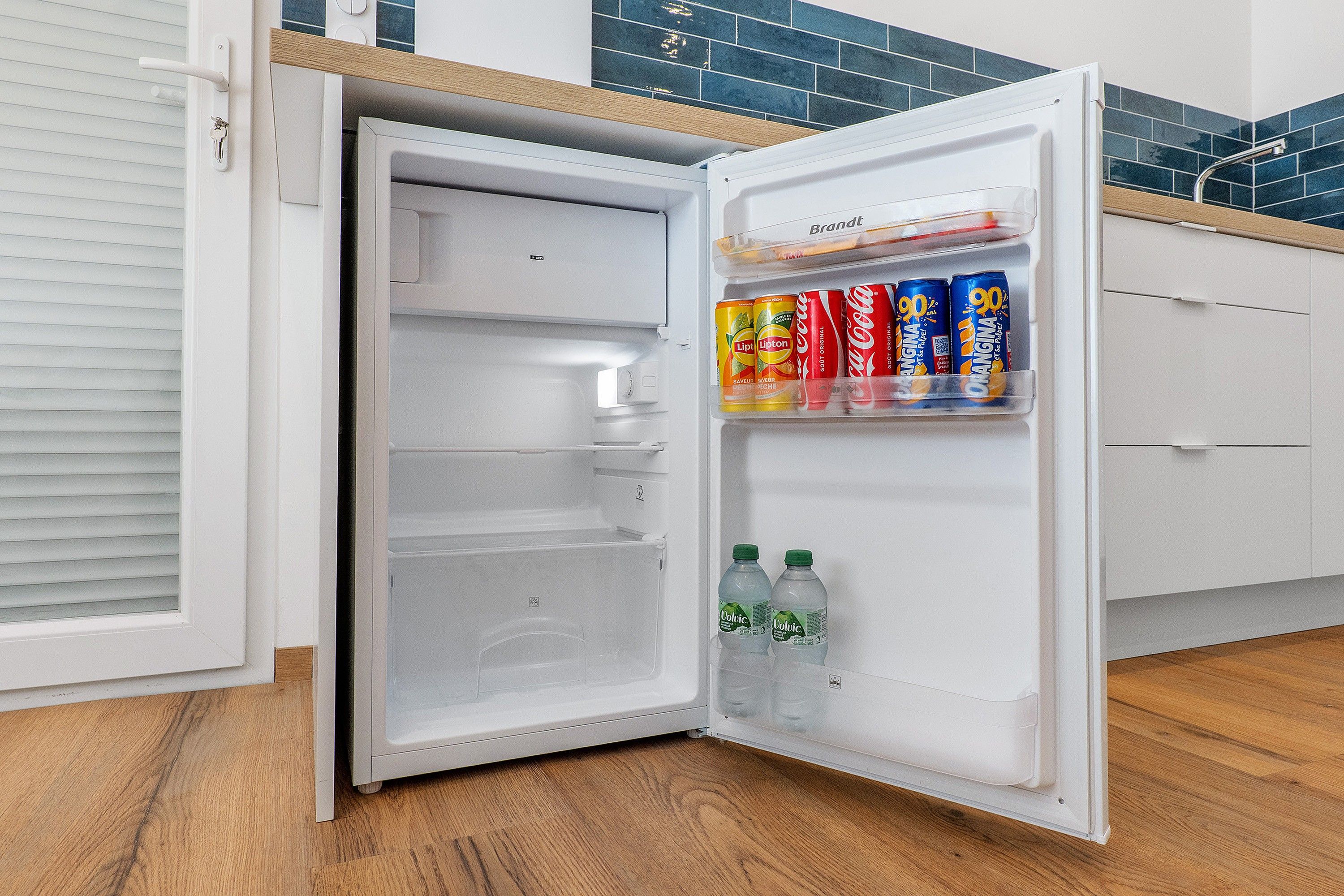 Un réfrigérateur ouvert, doté d’un compartiment congélateur et d’une étagère contenant des boissons.