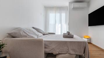 Une chambre à coucher moderne, avec un lit, une chaise, une table de chevet avec une lampe et une grande fenêtre avec des rideaux.