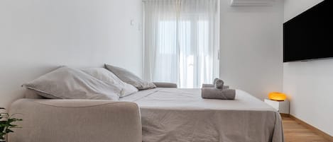 A modern bedroom with a bed, a chair, a bedside table with a lamp, and a large window with curtains.