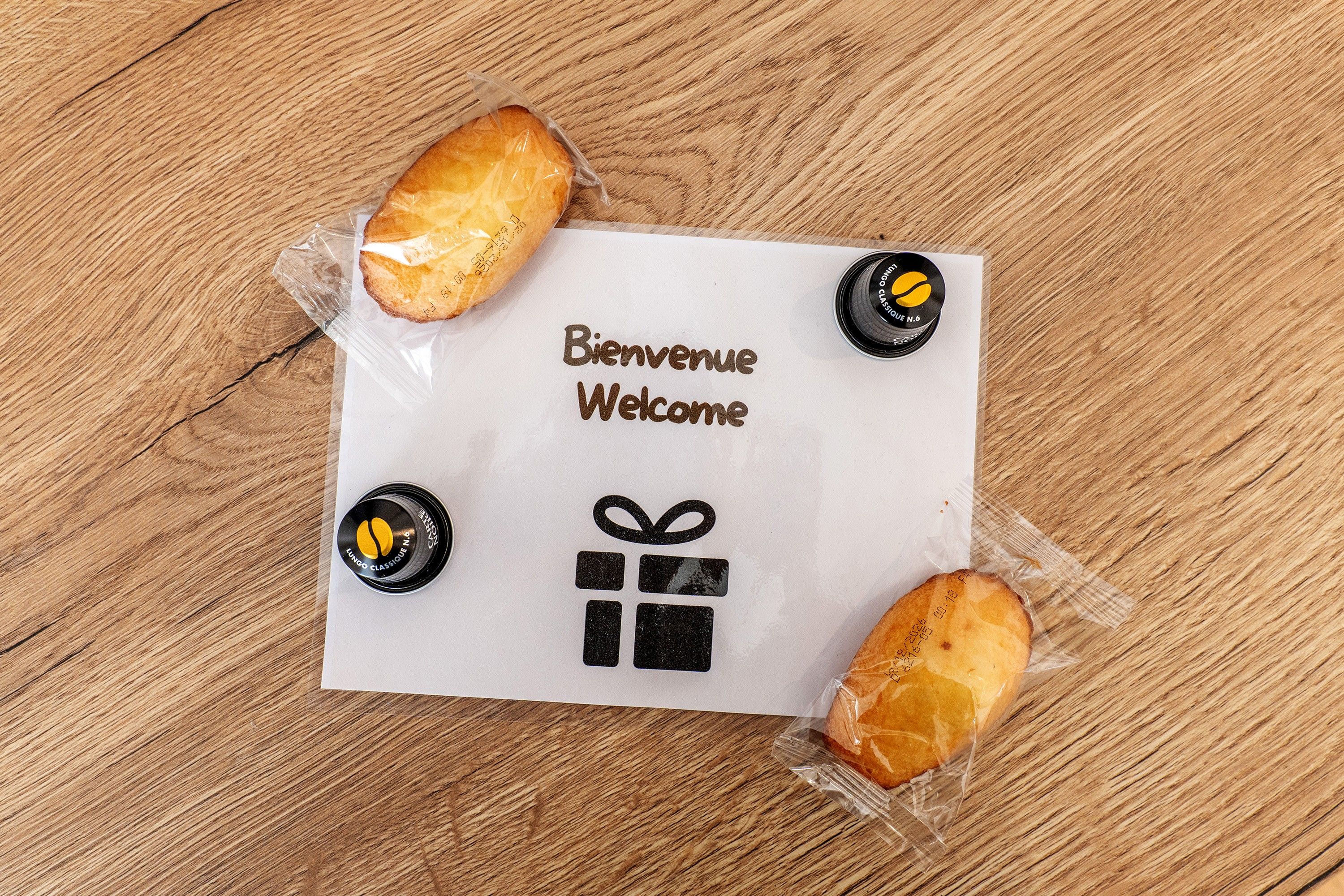 A welcome sign with a gift icon and two coffee cups on a wooden surface.