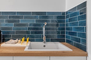 A modern kitchen with a white sink, dark blue tiles, and a wooden countertop.