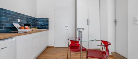 Eine moderne Küche mit weißen Schränken, einer blauen Fliesenrückwand und einer Holz Arbeitsplatte. Es steht ein Glastisch mit zwei roten Stühlen sowie ein roter Stuhl mit Metallgestell da.