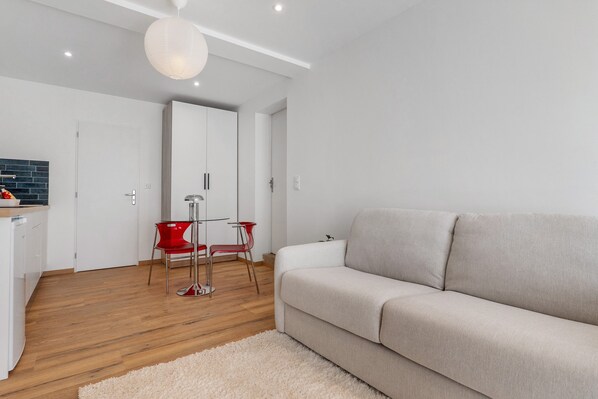 A modern living room with a sofa, a red chair, a white door, and a wooden floor.