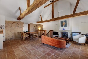 A rustic interior with exposed wooden beams, a stone wall, a fireplace, and a dining area with wicker furniture. - 'Château Les Forges -Tennis, Pool, Golf '  (Les Forges)