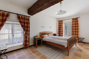 A bedroom with a wooden bed, a nightstand, a desk, a window with curtains, and a hanging light fixture.