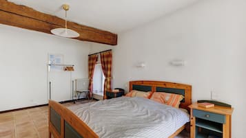Une chambre à coucher avec un lit en bois, une table de chevet, une commode, un radiateur, une fenêtre avec des rideaux et un ventilateur de plafond.